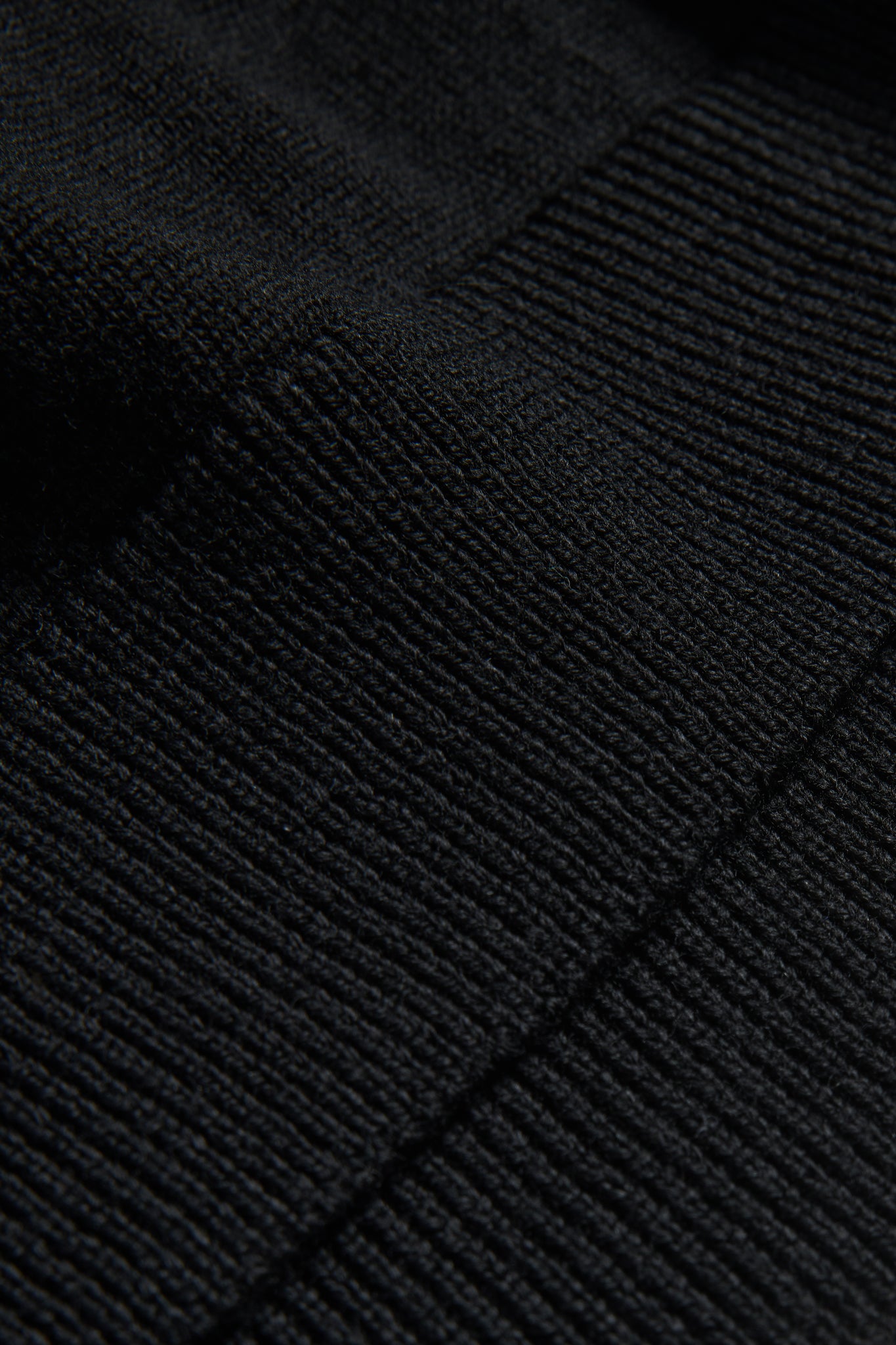 Unisex knit crewneck, black mulesing-free merino wool, close-up of fine rib-knit texture.