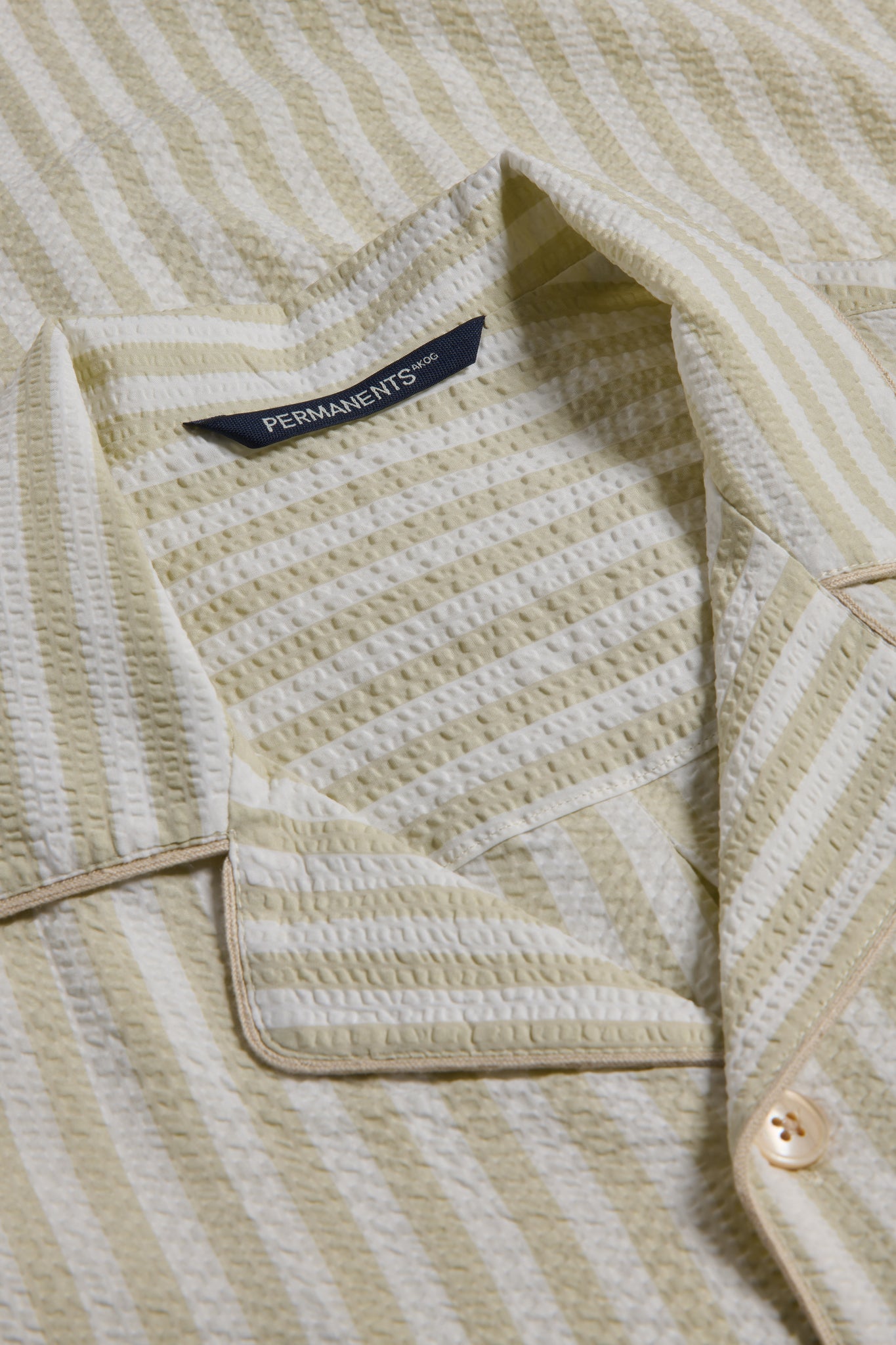 Unisex pyjama set, organic cotton seersucker, sage stripe, piped trim, close-up of collar and button.
