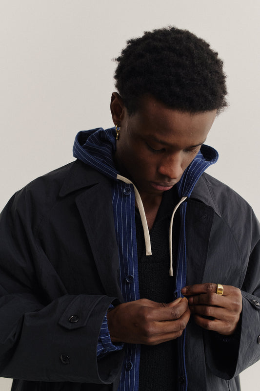 Men's outerwear, oversized navy recycled nylon-cotton blend Serrara Mac jacket with reverse collar, worn over a striped hoodie.