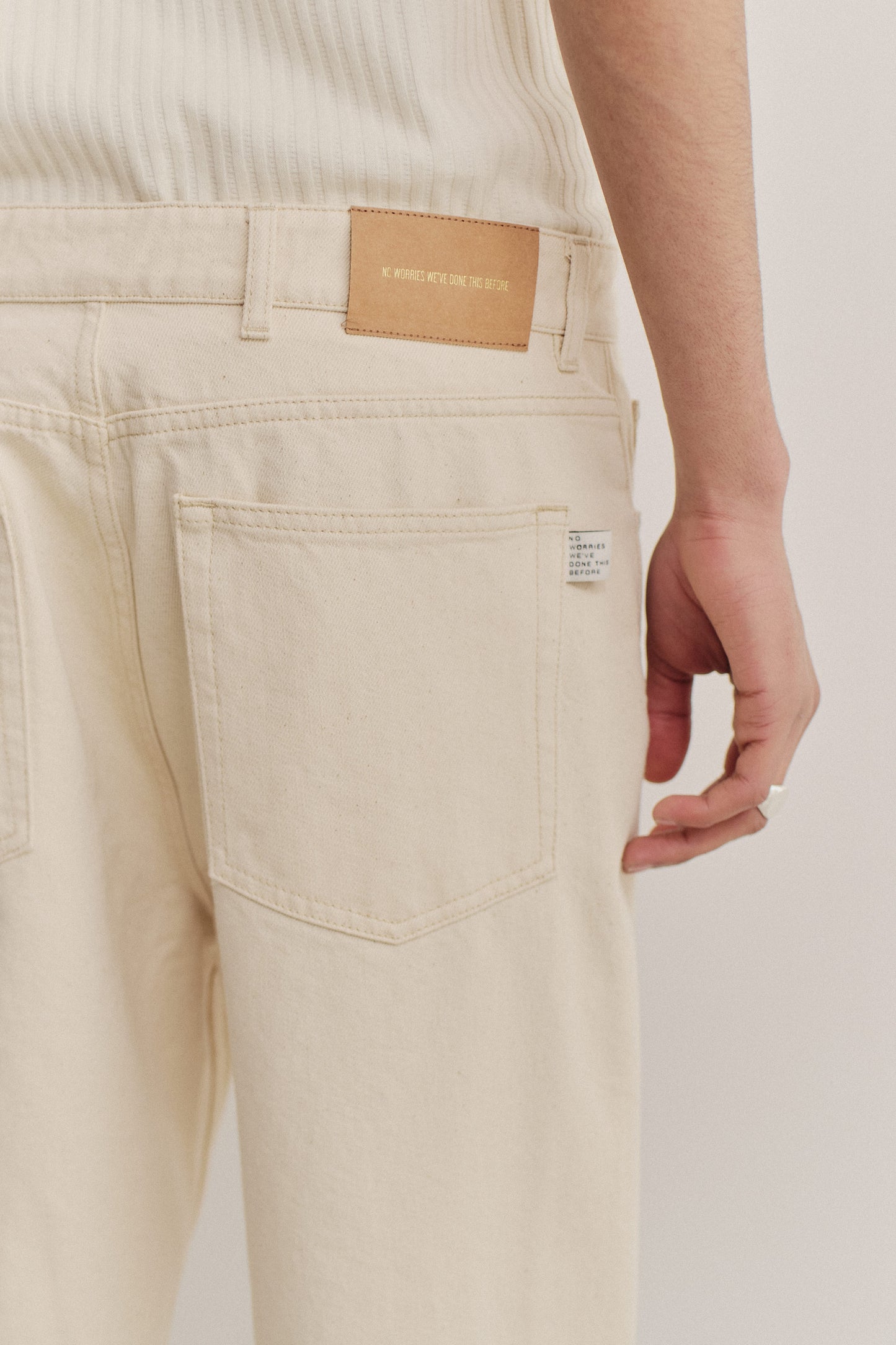 Men's long-pants, organic cotton raw denim, off-white, with a leather patch and back pocket.