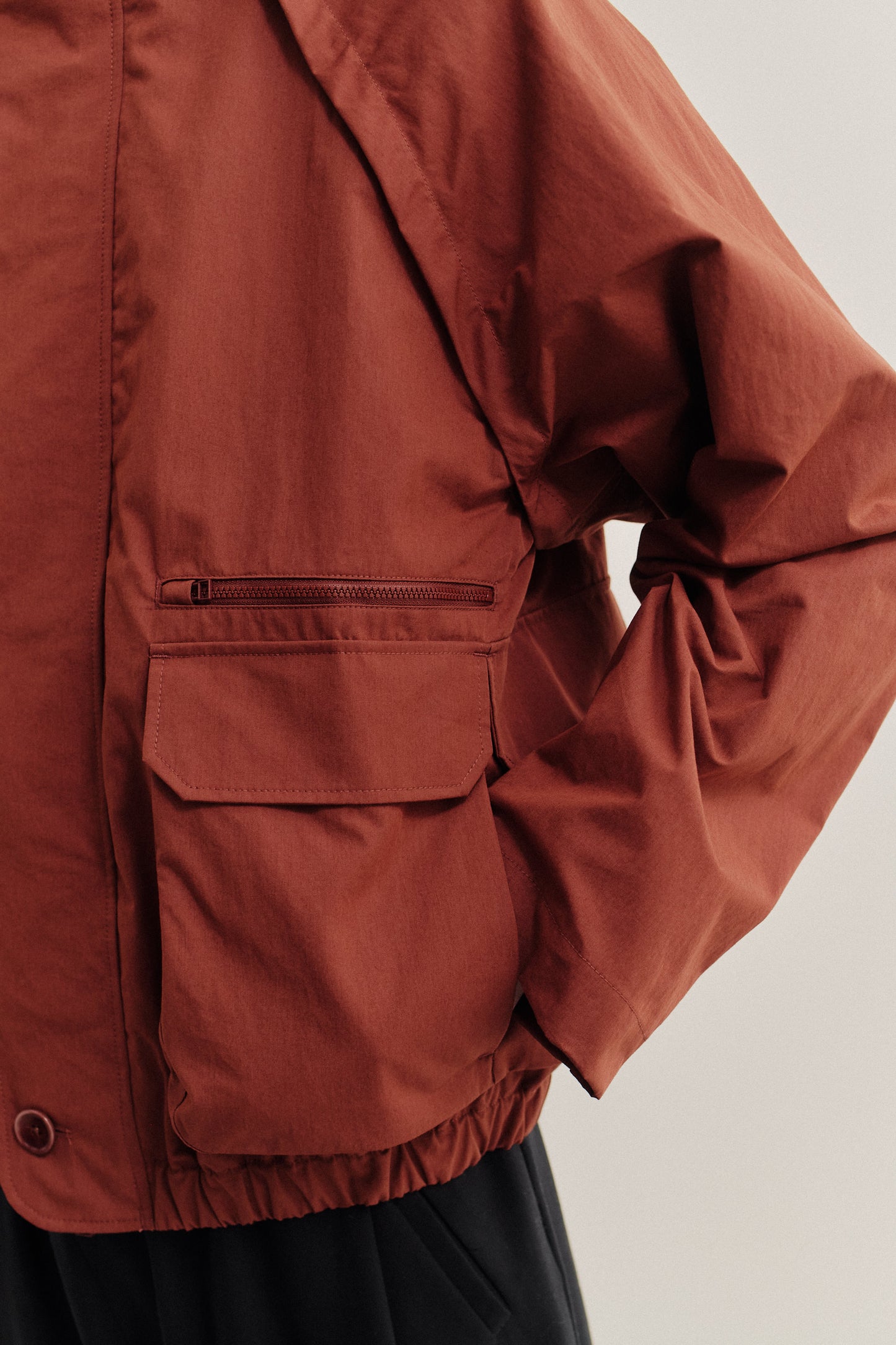 Men's outerwear jacket, rust cotton blend, wide silhouette, deep raglan sleeves, zip-off arms, bellows pockets.