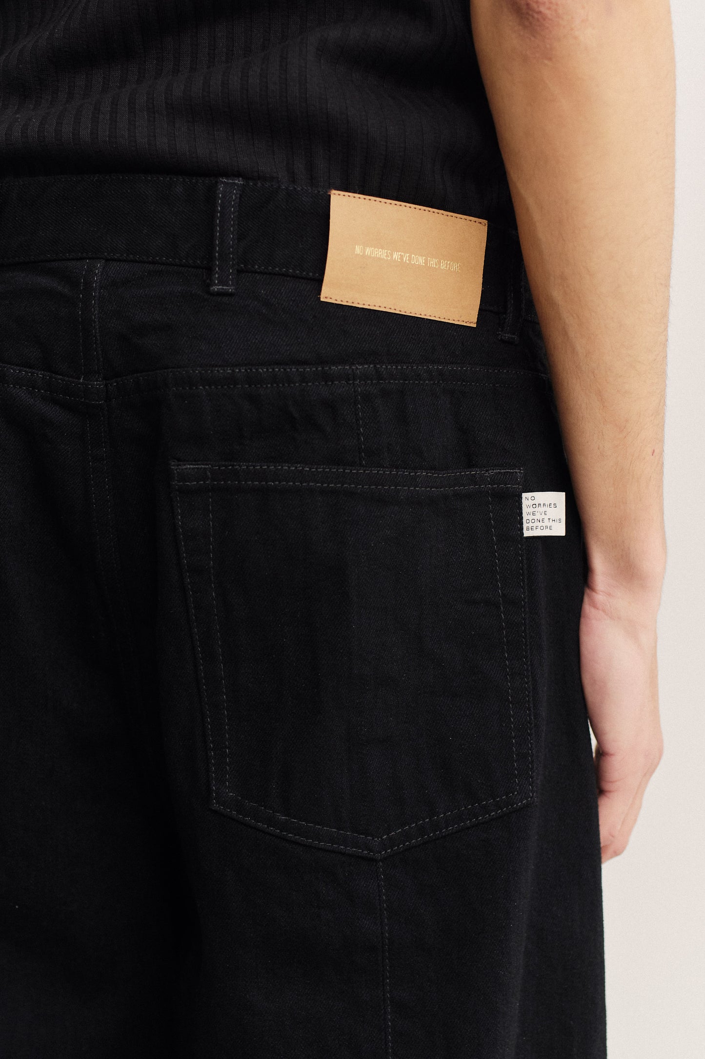 Men's long-pants, cotton selvedge denim, black, with a tan leather patch and white fabric label on the back.