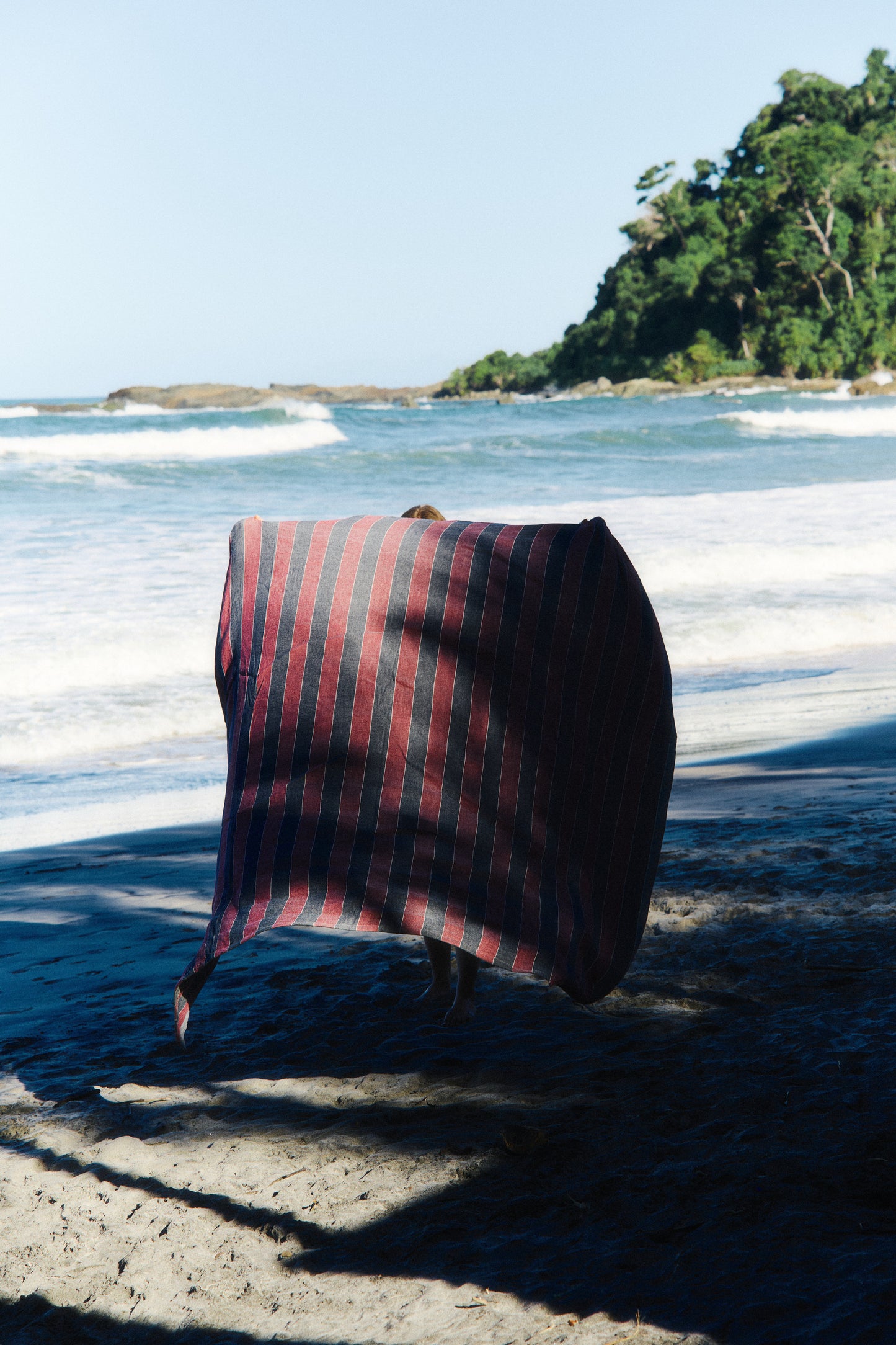 Accessories beach towel, red and navy striped linen-cotton blend, on a sunny beach.
